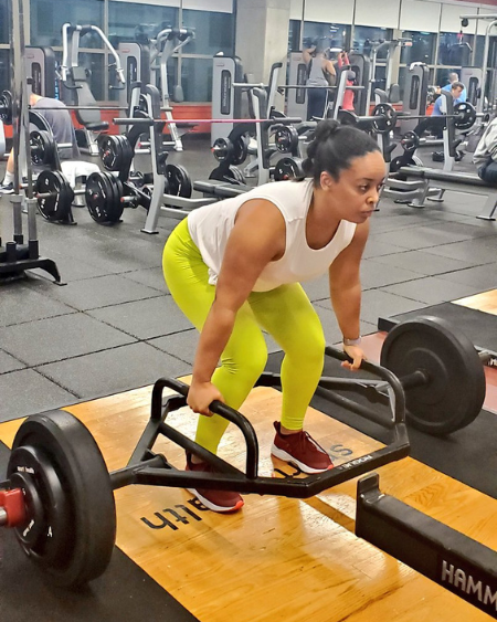 Woman lifting heavy weights while wearing Fabletics and a slicked back ponytail. 