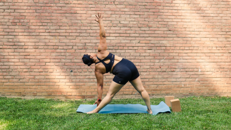 Black woman in trikonasana - triangle pose - outdoors on a yoga mat