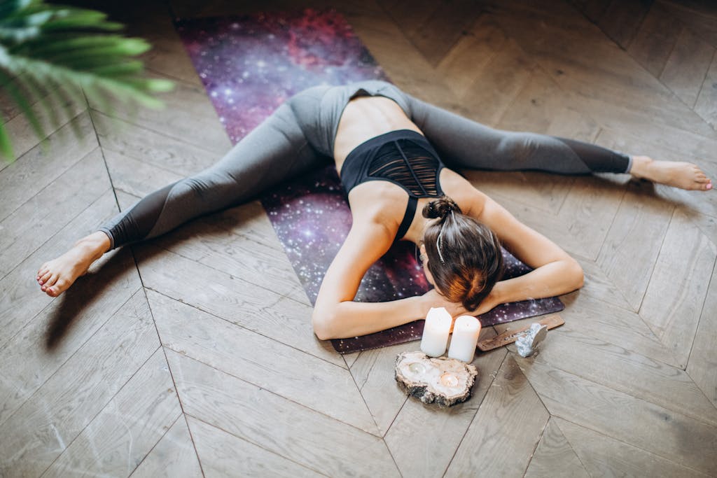 Woman in yoga pose indoors with candles and yoga mat, promoting relaxation and mindfulness.